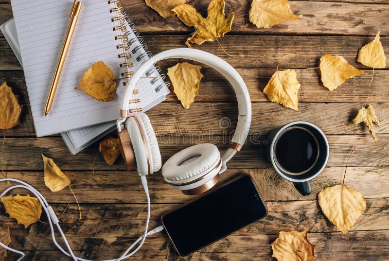 Headphones with autumn dry leaves, cuo of coffee and notepads on rustic wooden background. Top view. Flat lay. Headphones with autumn dry leaves, cuo of coffee and notepads on rustic wooden background. Top view. Flat lay