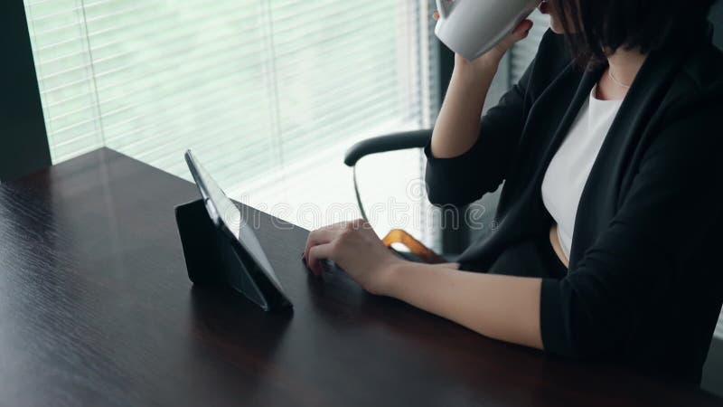 Służąca siedząca za biurkiem przy użyciu tabletu do wpisywania wiadomości służbowej Młody przedsiębiorca pracuje w biurze