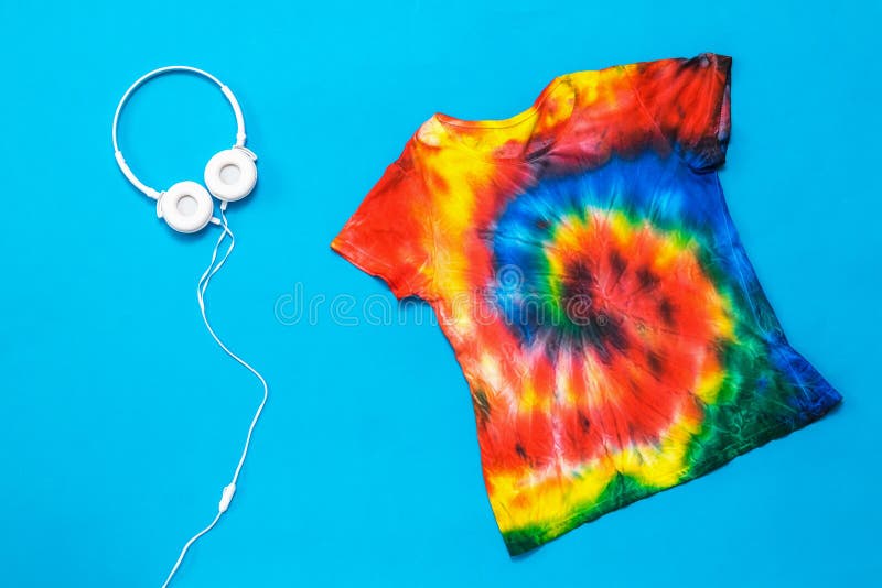 T-shirt in the style of tie dye and white headphones on a blue background. Flat lay. Pastel color.