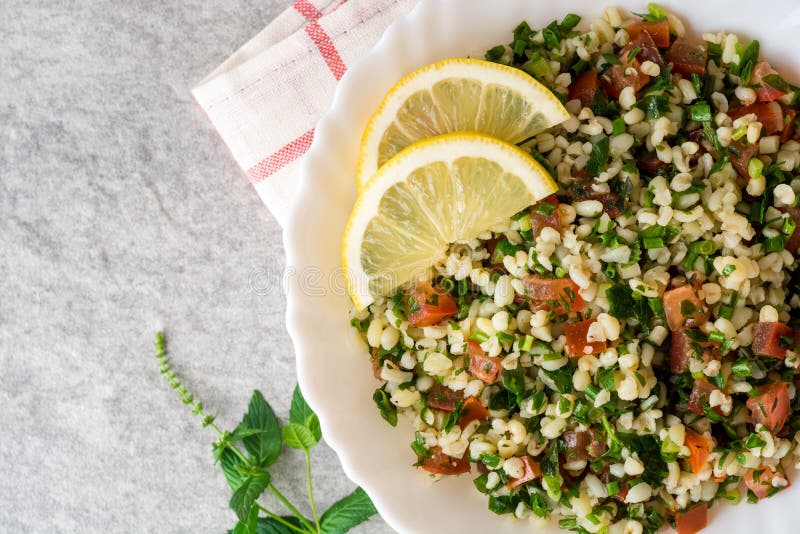 Tabboulehsalade met bulgur, tomaten, peterselie, groene ui en munt in plaat op grijze steenlijst royalty-vrije stock foto Tabboulehsalade met bulgur, tomaten, peterselie, groene ui en munt in plaat op grijze steenlijst royalty-vrije stock foto