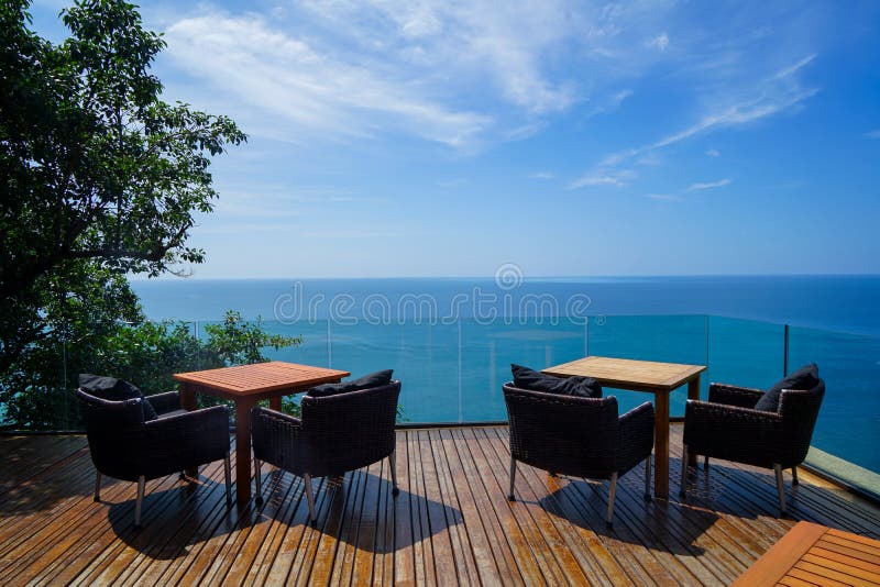 Tabelle e poltrone all'aperto del rattan che mettono sulla piattaforma e sul balcone di legno con la vista panoramica del mare de fotografia stock libera da diritti Tabelle e poltrone all'aperto del rattan che mettono sulla piattaforma e sul balcone di legno con la vista panoramica del mare de fotografia stock libera da diritti