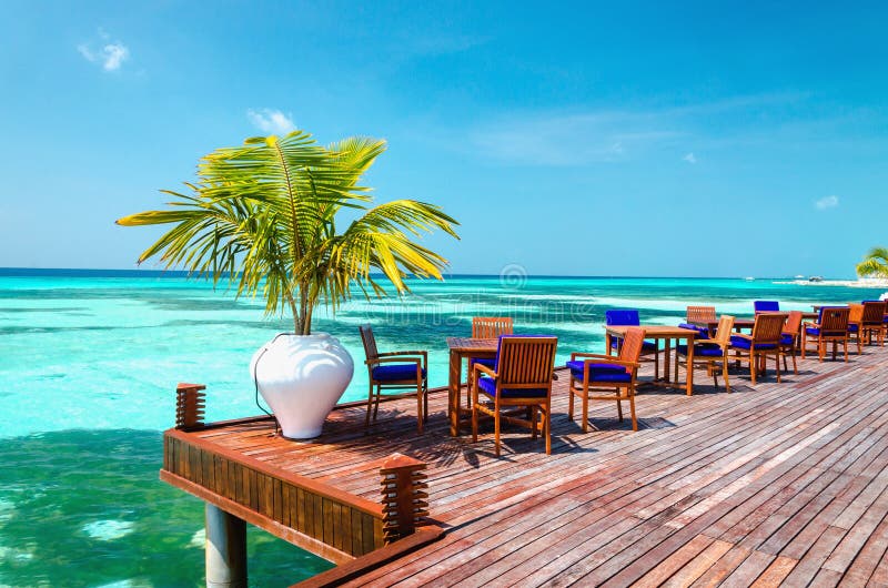 Tabelle und Stühle am Wasserrestaurant am Hintergrund des blauen Himmels, Malediven-Insel stockbild Tabelle und Stühle am Wasserrestaurant am Hintergrund des blauen Himmels, Malediven-Insel stockbild