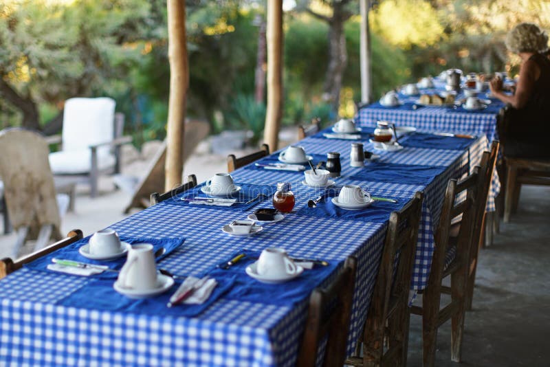 Tabla con las placas y las tazas de café vacías, mantel a cuadros azul, persona borrosa en el fondo que tiene mañana imagen de archivo libre de regalías Tabla con las placas y las tazas de café vacías, mantel a cuadros azul, persona borrosa en el fondo que tiene mañana imagen de archivo libre de regalías