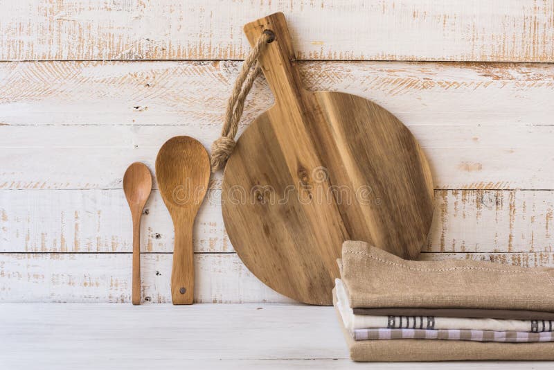 Tabla de cortar redonda de madera, cucharas, pila de toallas de cocina de lino en el fondo blanco de madera del tablón fotografía de archivo Tabla de cortar redonda de madera, cucharas, pila de toallas de cocina de lino en el fondo blanco de madera del tablón fotografía de archivo