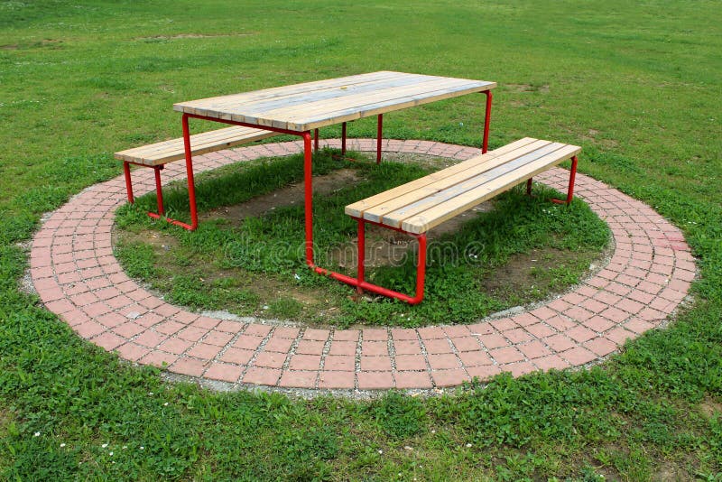 Tabla del parque público conectada con dos bancos hechos de la madera dilapidada y del metal rodeados con las tejas de piedra dec imágenes de archivo libres de regalías Tabla del parque público conectada con dos bancos hechos de la madera dilapidada y del metal rodeados con las tejas de piedra dec imágenes de archivo libres de regalías