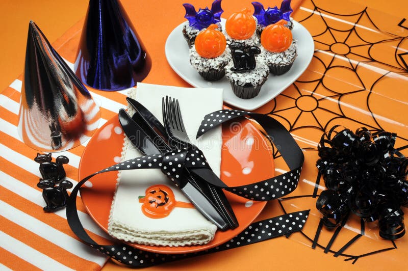 Happy Halloween party table with orange polka dot plates an chocolate cupcakes with black cat, pumpkin and bats decorations on orange background. Happy Halloween party table with orange polka dot plates an chocolate cupcakes with black cat, pumpkin and bats decorations on orange background.