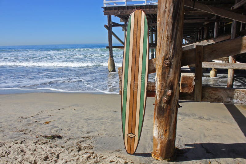 Tabla hawaiana de madera contra el embarcadero de la playa de California