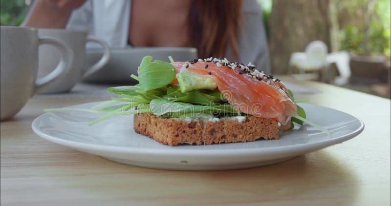Table cafe plate is appetizing toast with salmon and herbs - ideal option for breakfast. In background, visitor is
