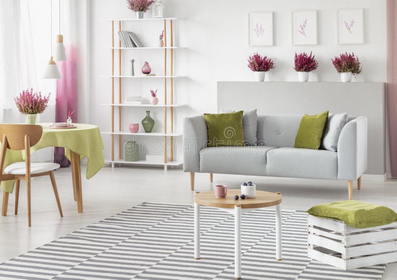 Dining table with olive green tablecloth in bright scandinavian living room with white and wooden furniture, grey sofa and striped carpet , real photo. Dining table with olive green tablecloth in bright scandinavian living room with white and wooden furniture, grey sofa and striped carpet , real photo