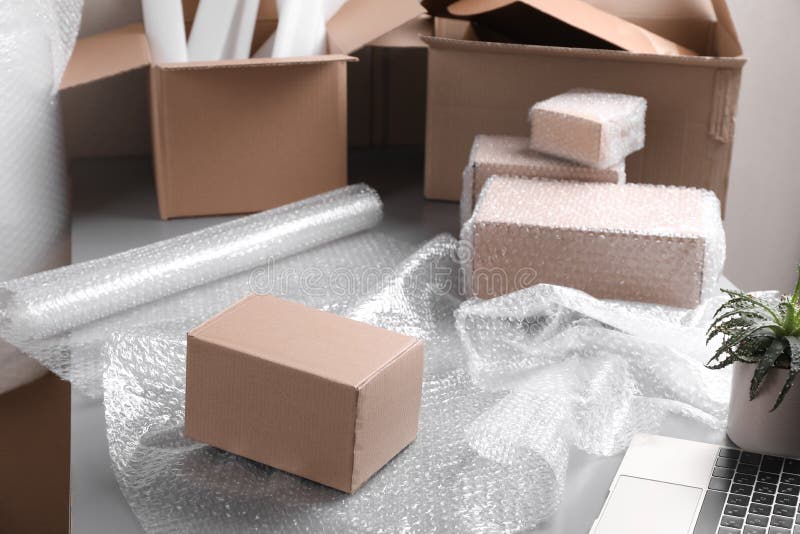 Table with Laptop, Boxes and Bubble Wrap in Warehouse Stock Image