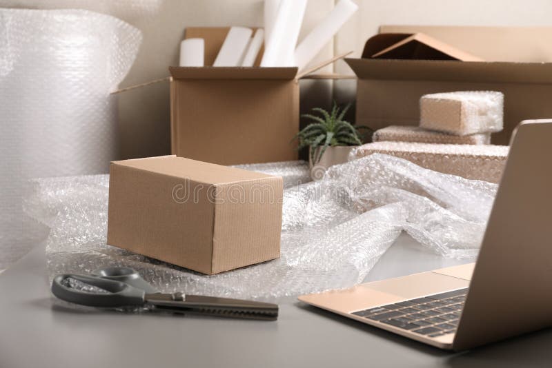 Table with Laptop, Boxes and Bubble Wrap in Warehouse Stock Image