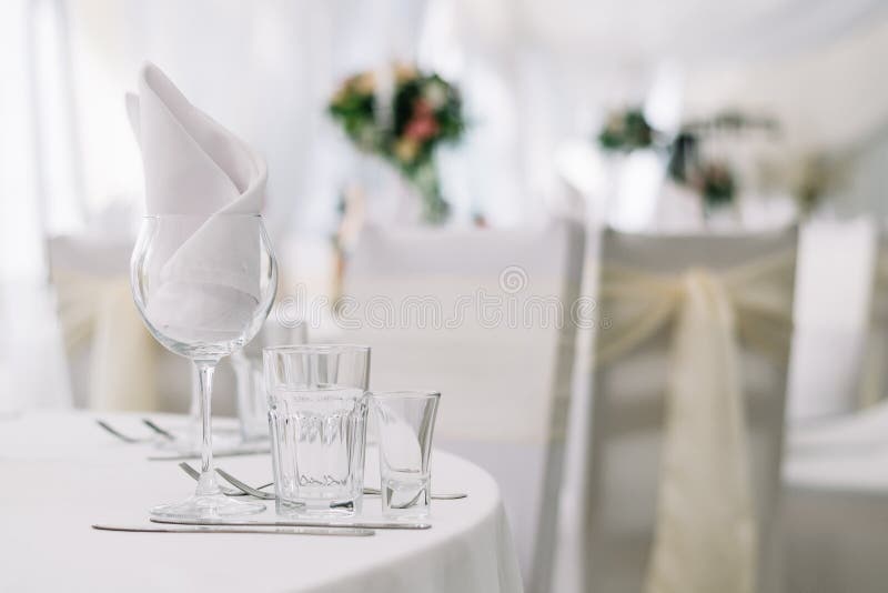 Table set for an event party or wedding reception on white tablecloth. White soft background with tables and flowers.