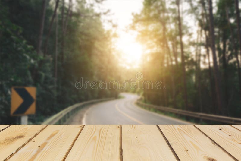 Table vide de conseil en bois devant le fond brouillé Du bois brun de perspective au-dessus de la route est entouré par la forêt images stock Table vide de conseil en bois devant le fond brouillé Du bois brun de perspective au-dessus de la route est entouré par la forêt images stock