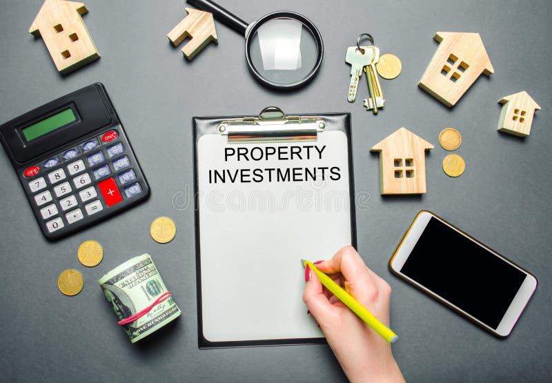 Table with wooden houses, calculator, coins, magnifying glass with the word Property investments. Attracting investment in your