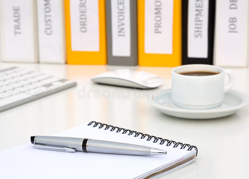 White Office Table with Notepad Executive Class Grey Metal Pen Coffee Computer Keyboard and many Folders with Business Terms Titles on Background Side View. White Office Table with Notepad Executive Class Grey Metal Pen Coffee Computer Keyboard and many Folders with Business Terms Titles on Background Side View