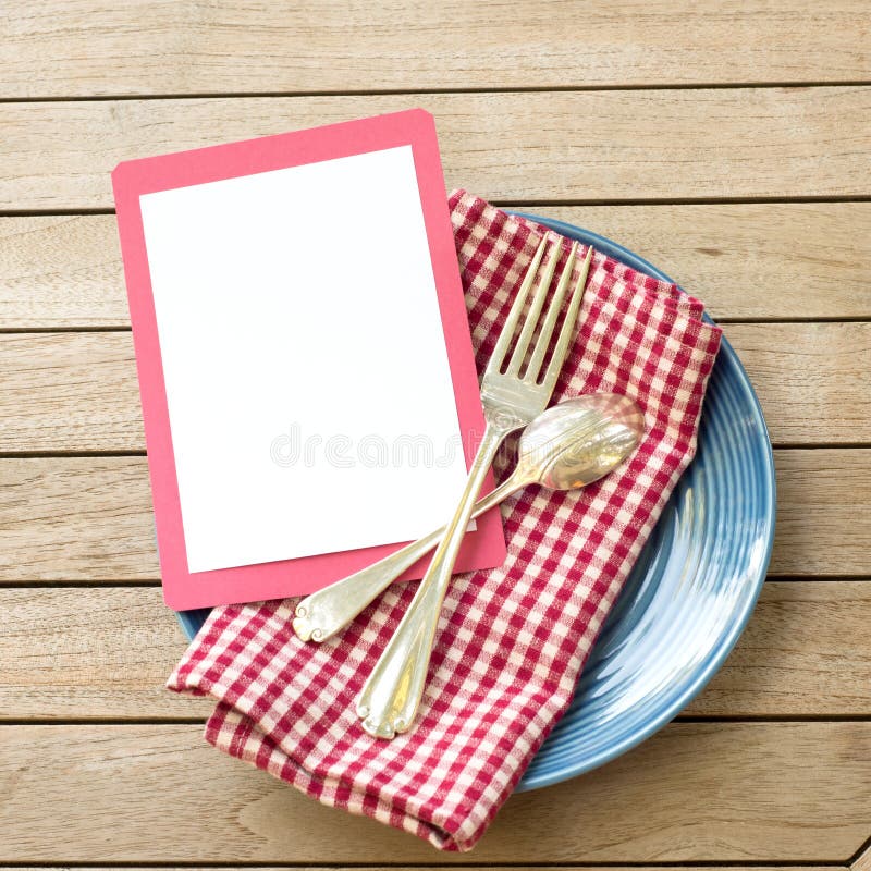 Summer Picnic Outdoor Table Placesetting with Red White and Blue Colors with fork and spoon with a Blank Card for your words, text, copy or design. A flat lay and square crop from top down view. Summer Picnic Outdoor Table Placesetting with Red White and Blue Colors with fork and spoon with a Blank Card for your words, text, copy or design. A flat lay and square crop from top down view