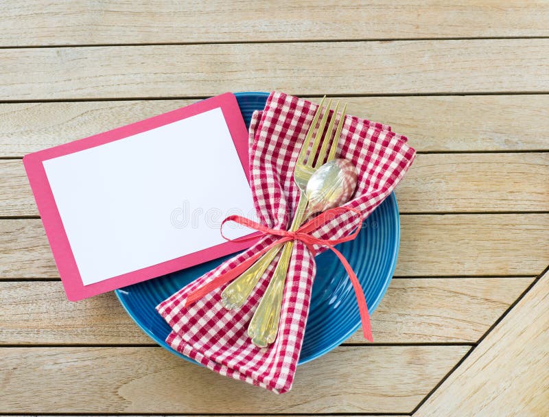 Summer Picnic Outdoor Table Placesetting with Red White and Blue Colors with fork and spoon with a Blank Card for your words, text, copy or design. A flat lay and horizontal crop from top down view. Summer Picnic Outdoor Table Placesetting with Red White and Blue Colors with fork and spoon with a Blank Card for your words, text, copy or design. A flat lay and horizontal crop from top down view