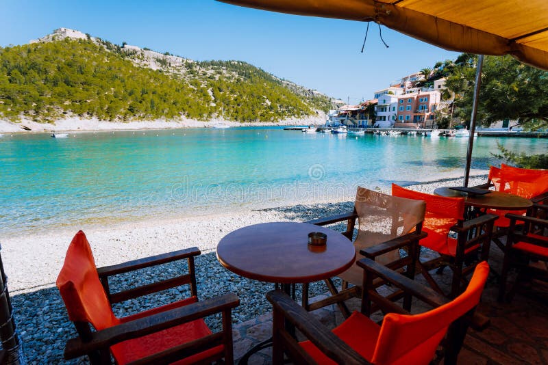 Tables with chairs of cozy Greek tavern restaurant in front of the beach in Assos village on Kefalonia island in Greece. On summer morning royalty free stock images Tables with chairs of cozy Greek tavern restaurant in front of the beach in Assos village on Kefalonia island in Greece. On summer morning royalty free stock images