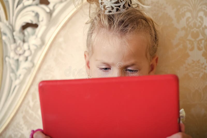 Tableta roja del uso del niño de la muchacha en el sofá foto de archivo libre de regalías Tableta roja del uso del niño de la muchacha en el sofá foto de archivo libre de regalías