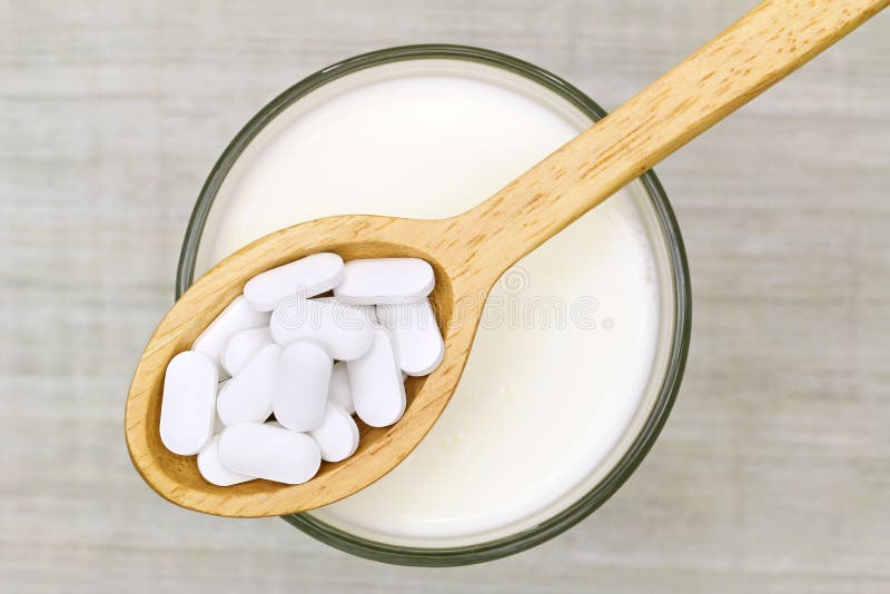 Top view of a wooden spoon of white Calcium carbonate tablets above a glass of fresh milk on a gray background. Top view of a wooden spoon of white Calcium carbonate tablets above a glass of fresh milk on a gray background