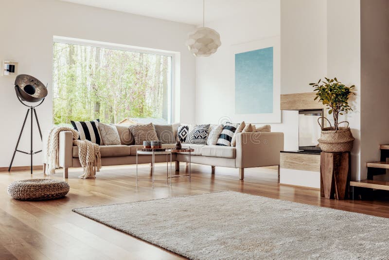 Tabouret en osier et un lampadaire industriel dans un intérieur lumineux de salon avec le décor chic et les éléments en bois photo libre de droits Tabouret en osier et un lampadaire industriel dans un intérieur lumineux de salon avec le décor chic et les éléments en bois photo libre de droits