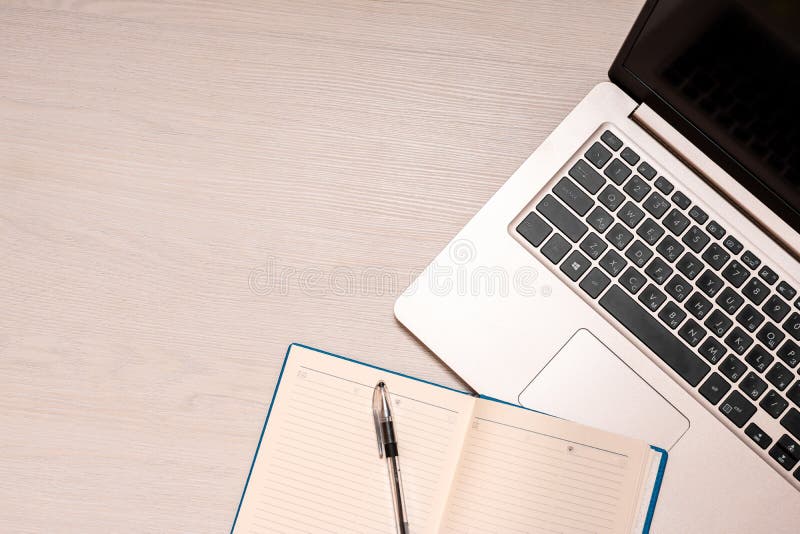 Taccuino aperto con la penna nera ed il computer portatile d'argento su una tavola di legno bianca, vista superiore, spase della immagini stock
