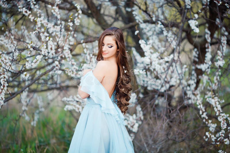 Tacto de la primavera La mujer joven hermosa feliz en vestido azul disfruta de las flores frescas y de la luz del sol en parque d fotografía de archivo libre de regalías Tacto de la primavera La mujer joven hermosa feliz en vestido azul disfruta de las flores frescas y de la luz del sol en parque d fotografía de archivo libre de regalías