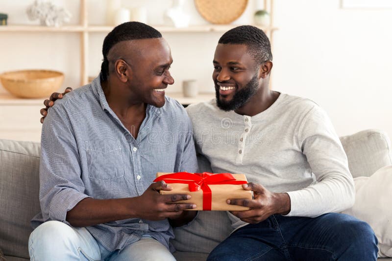 Tag der glücklichen Väter. Erwachsener schwarzer Sohn gratulierte seinem Seniorenvater Geschenk lizenzfreie stockbilder