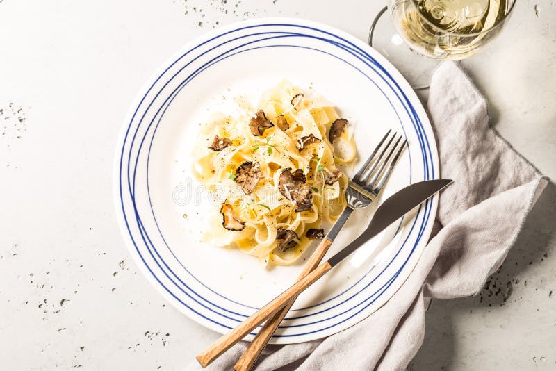 Tagliatelle pasta with black truffles and parmesan cheese. Plate captured from above top view, flat lay. Grey stone background. Layout with free text space