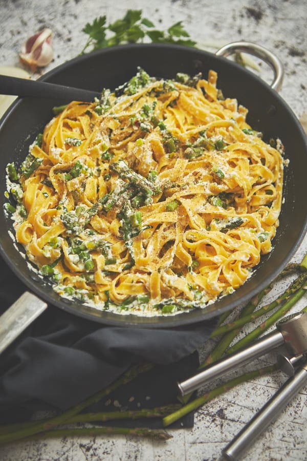 Tagliatelle pasta with ricotta cheese sauce and asparagus served on a black iron pan stock photo Tagliatelle pasta with ricotta cheese sauce and asparagus served on a black iron pan stock photo
