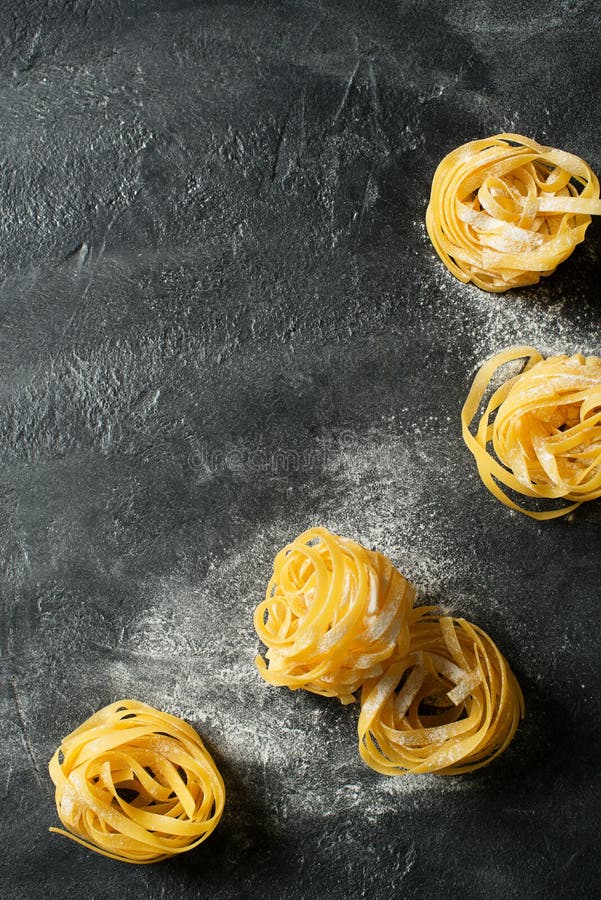Tagliatelle pasta uncooked, making spaghetti background, black texture