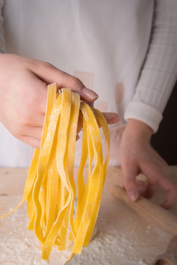 Tagliatelles faites maison crues italiennes fraîches de pâtes dans les mains d'une jeune femme Concept italien de pâtes image libre de droits Tagliatelles faites maison crues italiennes fraîches de pâtes dans les mains d'une jeune femme Concept italien de pâtes image libre de droits