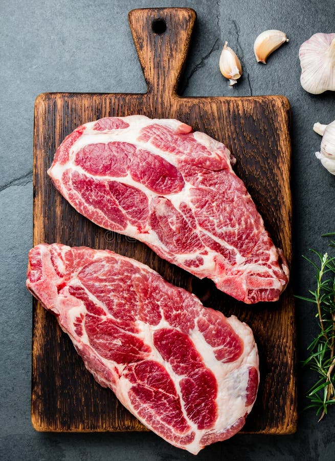Taglio crudo della cotoletta della carne di maiale per il BBQ della griglia con le erbe sul bordo di legno, fondo dell'ardesia, v fotografia stock Taglio crudo della cotoletta della carne di maiale per il BBQ della griglia con le erbe sul bordo di legno, fondo dell'ardesia, v fotografia stock