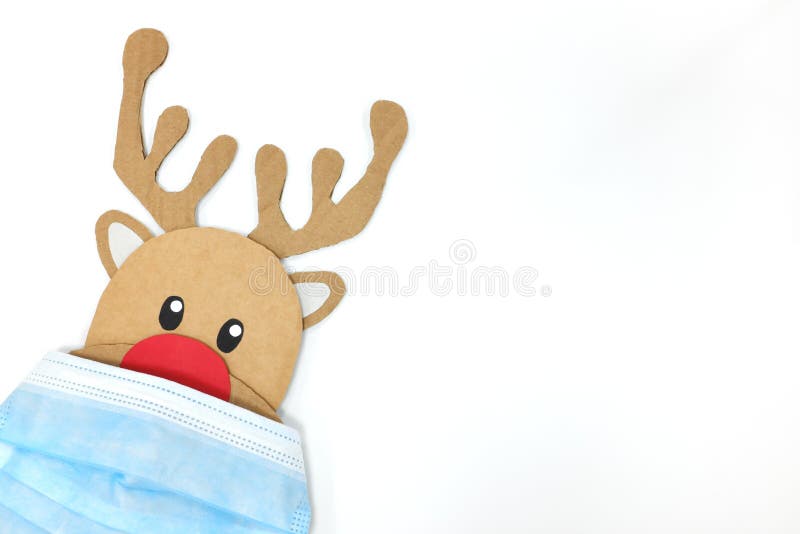 Taglio di cartone di rudolfo la renna rossa che sbircia mentre indossa una maschera. covid durante il periodo natalizio.
