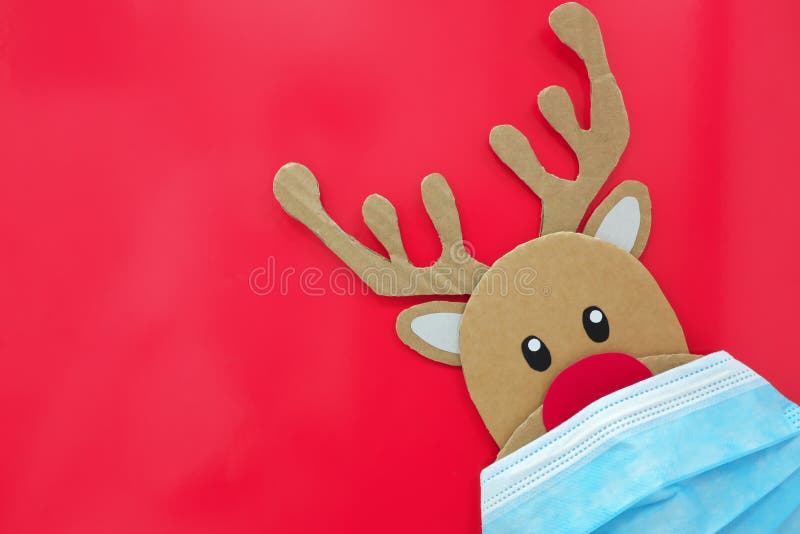 Taglio di cartone di rudolfo la renna rossa che sbircia mentre indossa una maschera. covid durante il periodo natalizio.