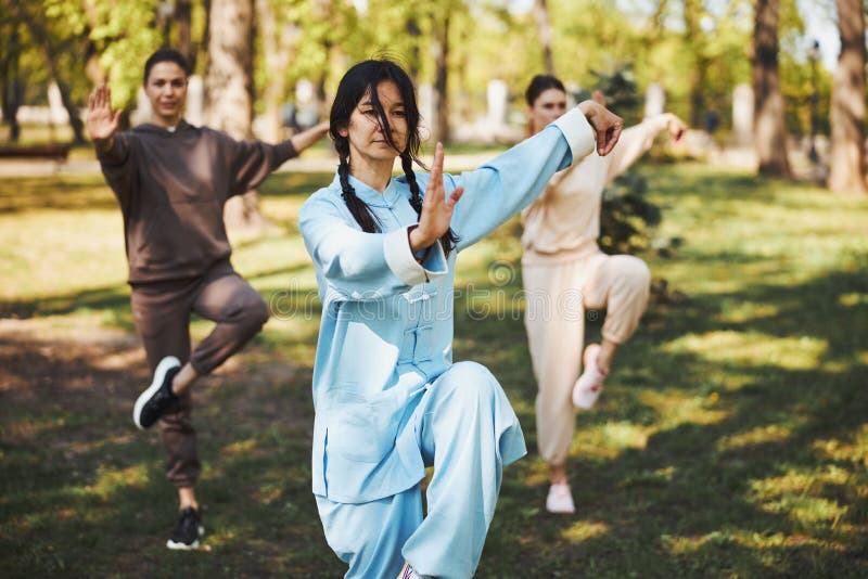Woman martial arts master staying on right leg outdoors while showing her palm to camera with pair of students. Qigong class stock images, royalty-free photos and pictures