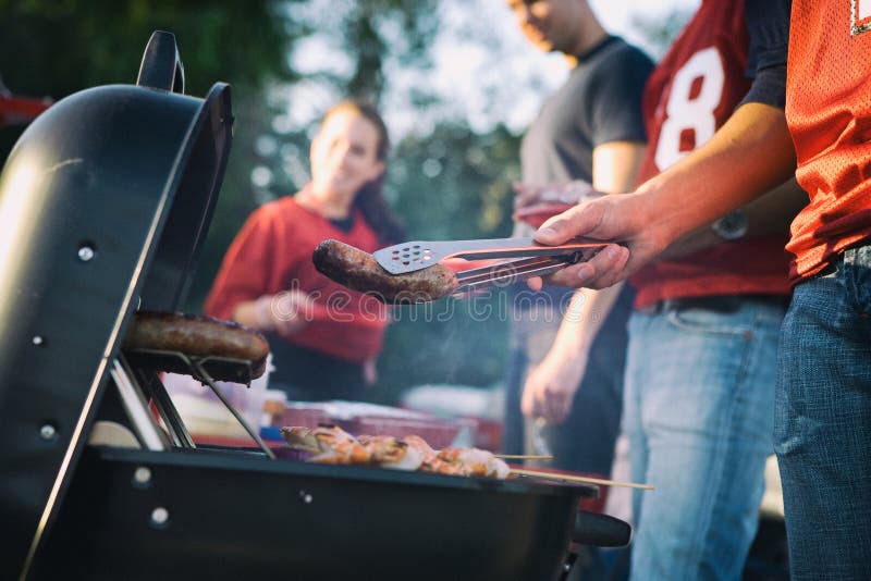 Tailgating: Άτομο που ψήνει τα λουκάνικα και άλλα τρόφιμα για Tailgate PA στη σχάρα στοκ εικόνες