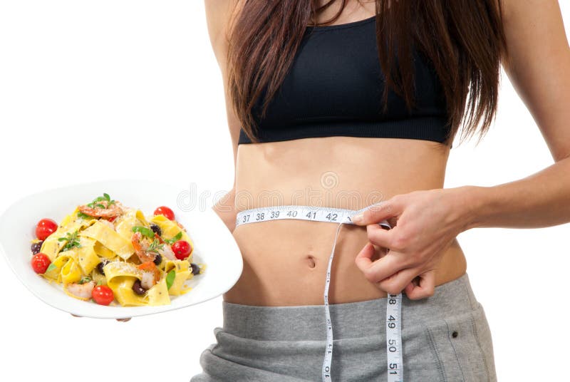 Young healthy slim girl measuring her waist with yellow tape measure, holding white plate with pappardelli, tagliatelli pasta, tomatoes, herbs, cheese on it , in hand on a white background. Young healthy slim girl measuring her waist with yellow tape measure, holding white plate with pappardelli, tagliatelli pasta, tomatoes, herbs, cheese on it , in hand on a white background
