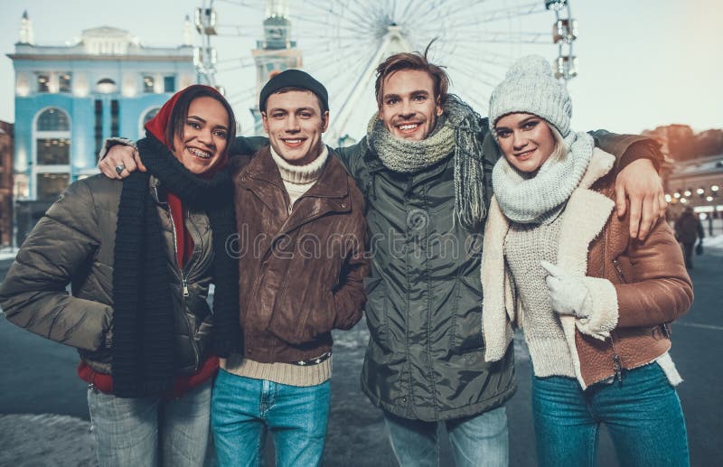 Taille de quatre jeunes amis se tenant dans des vêtements chauds dehors photo stock Taille de quatre jeunes amis se tenant dans des vêtements chauds dehors photo stock
