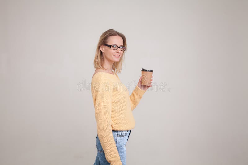 Taille-op portret die van de holdingskoffie GLB van de blondevrouw in haar handen en het glimlachen, de camera bekijken het drage stock foto Taille-op portret die van de holdingskoffie GLB van de blondevrouw in haar handen en het glimlachen, de camera bekijken het drage stock foto