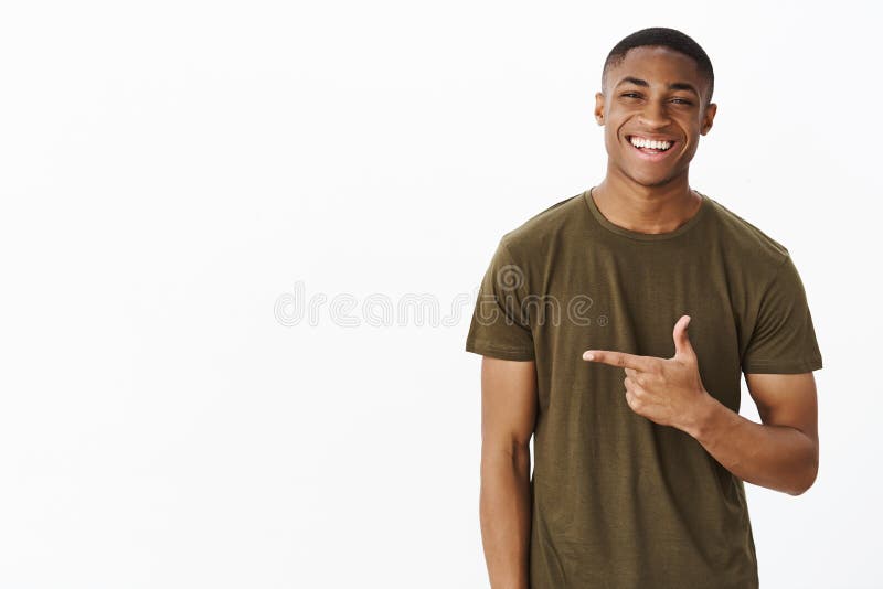 Taille- tirée du gentil et beau jeune homme gai d'afro-américain dirigeant la gauche avec l'index souriant et image stock