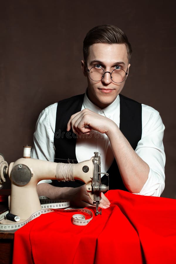 Tailor in Round Glasses Sits at a Table with a Sewing Machine Stock
