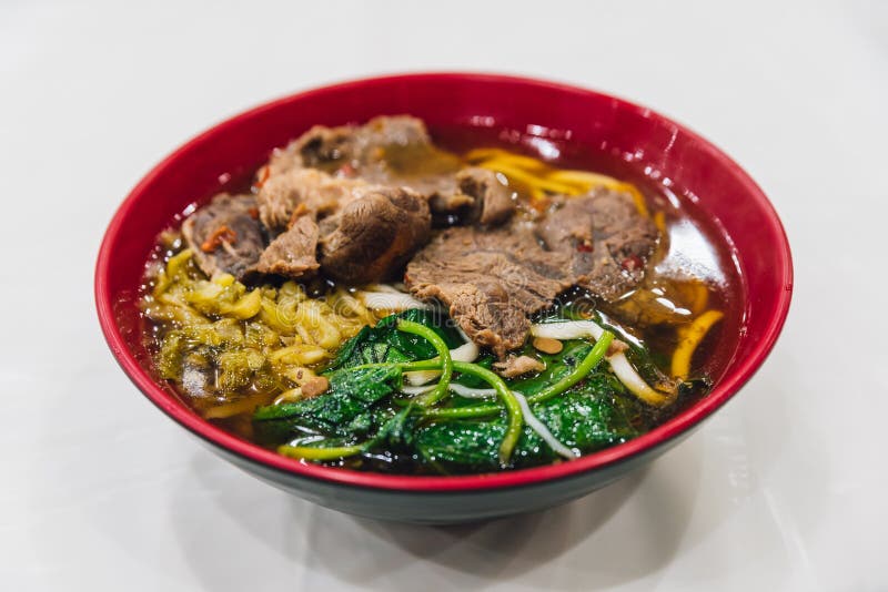 Taiwanese style beef noodle including sliced beef, flat egg noodle, sprouts, morning glory and soup in red bowl