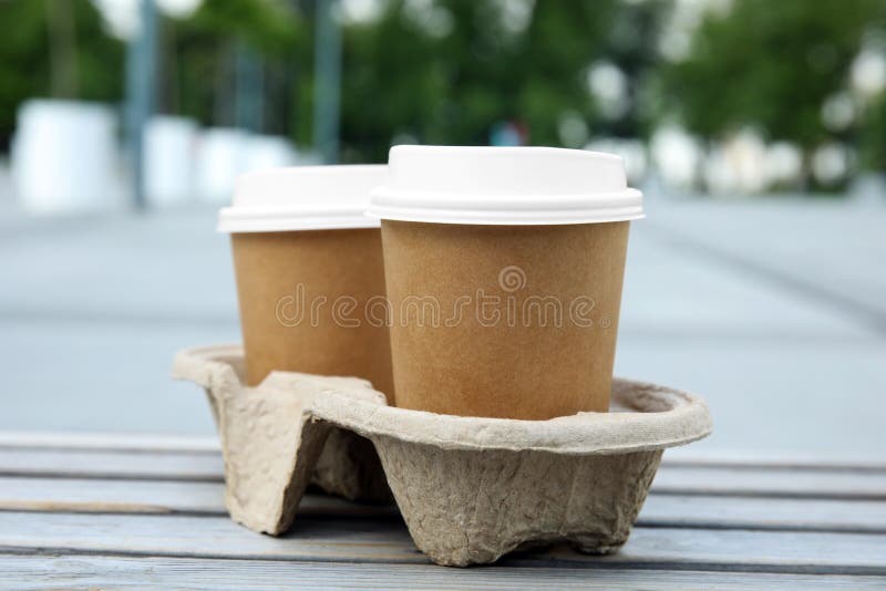 Takeaway paper coffee cups with plastic lids in cardboard holder on wooden bench outdoors royalty free stock image