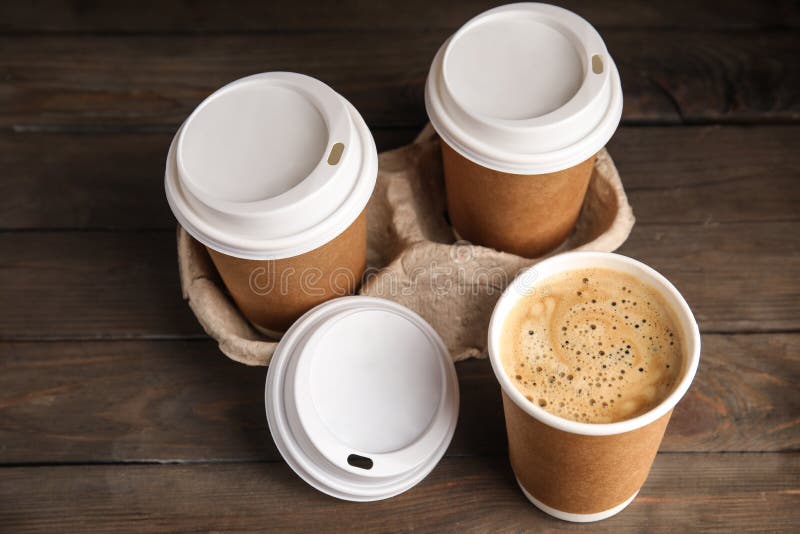 Takeaway paper coffee cups with plastic lids and cardboard holder on wooden table royalty free stock photo