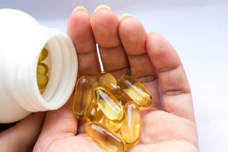 A white jar of fish oil in jelly-like transparent yellow capsules and a handful of capsules in a woman`s palm close-up on a white background. A white jar of fish oil in jelly-like transparent yellow capsules and a handful of capsules in a woman`s palm close-up on a white background