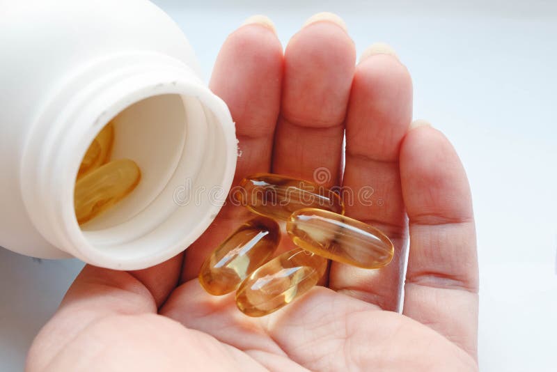 A white jar of fish oil in jelly-like transparent yellow capsules and a handful of capsules in a woman`s palm close-up on a white background. A white jar of fish oil in jelly-like transparent yellow capsules and a handful of capsules in a woman`s palm close-up on a white background