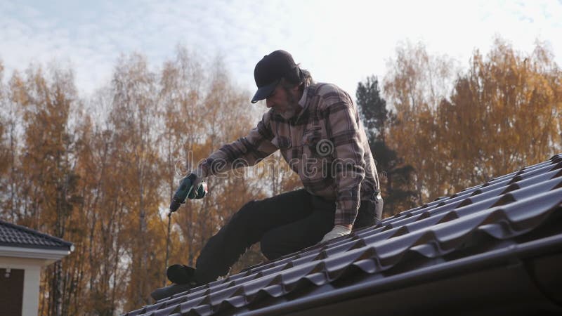 Takpannor använder en skruvmejsel för att dra åt takskruven i metalltaket.