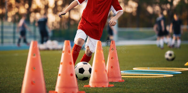 Soccer Drills: The Slalom Drill. Youth soccer practice drills. Young football player training on pitch. Soccer slalom cone drill. Boy in red soccer jersey shirt running with ball between cones. Soccer Drills: The Slalom Drill. Youth soccer practice drills. Young football player training on pitch. Soccer slalom cone drill. Boy in red soccer jersey shirt running with ball between cones