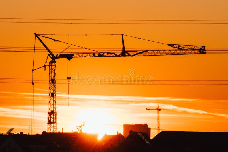 Tall construction crane silhouette in orange sky sunset shows construction site with engineering for modern buildings and city dev